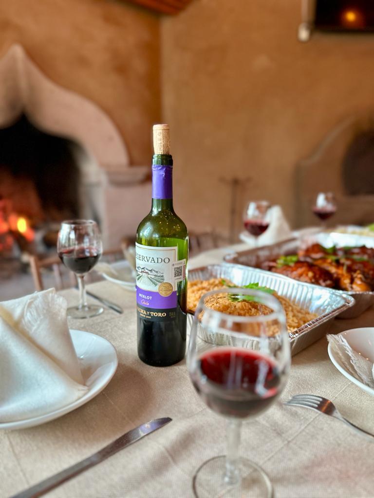 Mesa de cena romántica con vino tinto y chimenea encendida al fondo en ambiente rústico