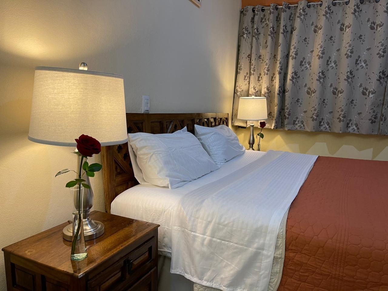 Habitación doble acogedora con cama matrimonial, lámparas cálidas y rosa roja decorativa